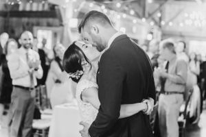 A couple shares a romantic first dance at their wedding reception while guests look on in black and white.