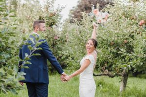 Two people celebrate joyfully while holding hands in a lush garden surrounded by flowering trees.