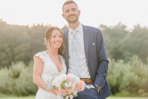 A bride and groom pose together outdoors at sunset, with the bride holding a pastel bouquet.