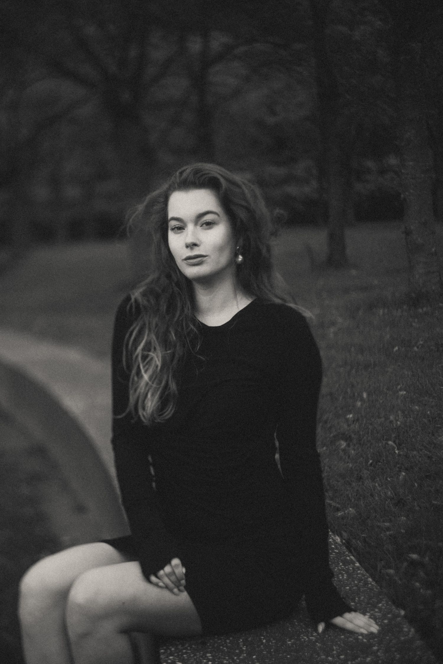 Moody black and white portrait series featuring velvet dress in natural setting.