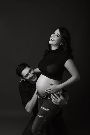 Black and white maternity photo capturing joyful moment between expectant parents.