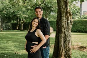 Outdoor maternity photo with couple embracing in sunny garden setting.