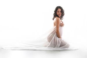 Artistic maternity portrait with flowing white fabric in bright studio setting.
