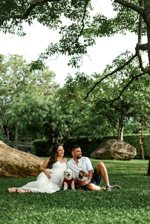 Couple with dog sitting on grass near large rocks in park setting.