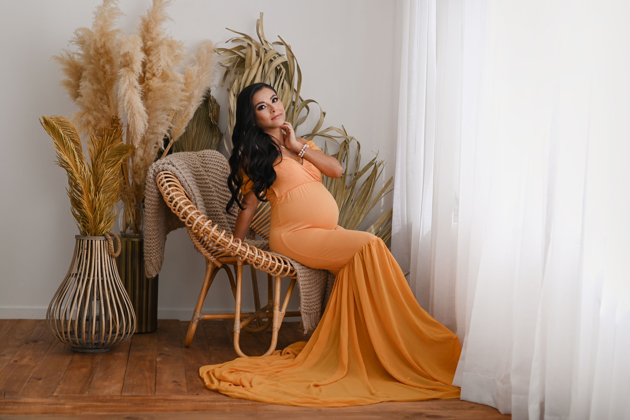Maternity portrait featuring an orange flowing dress and pampas grass decor in a bright minimalist setting.