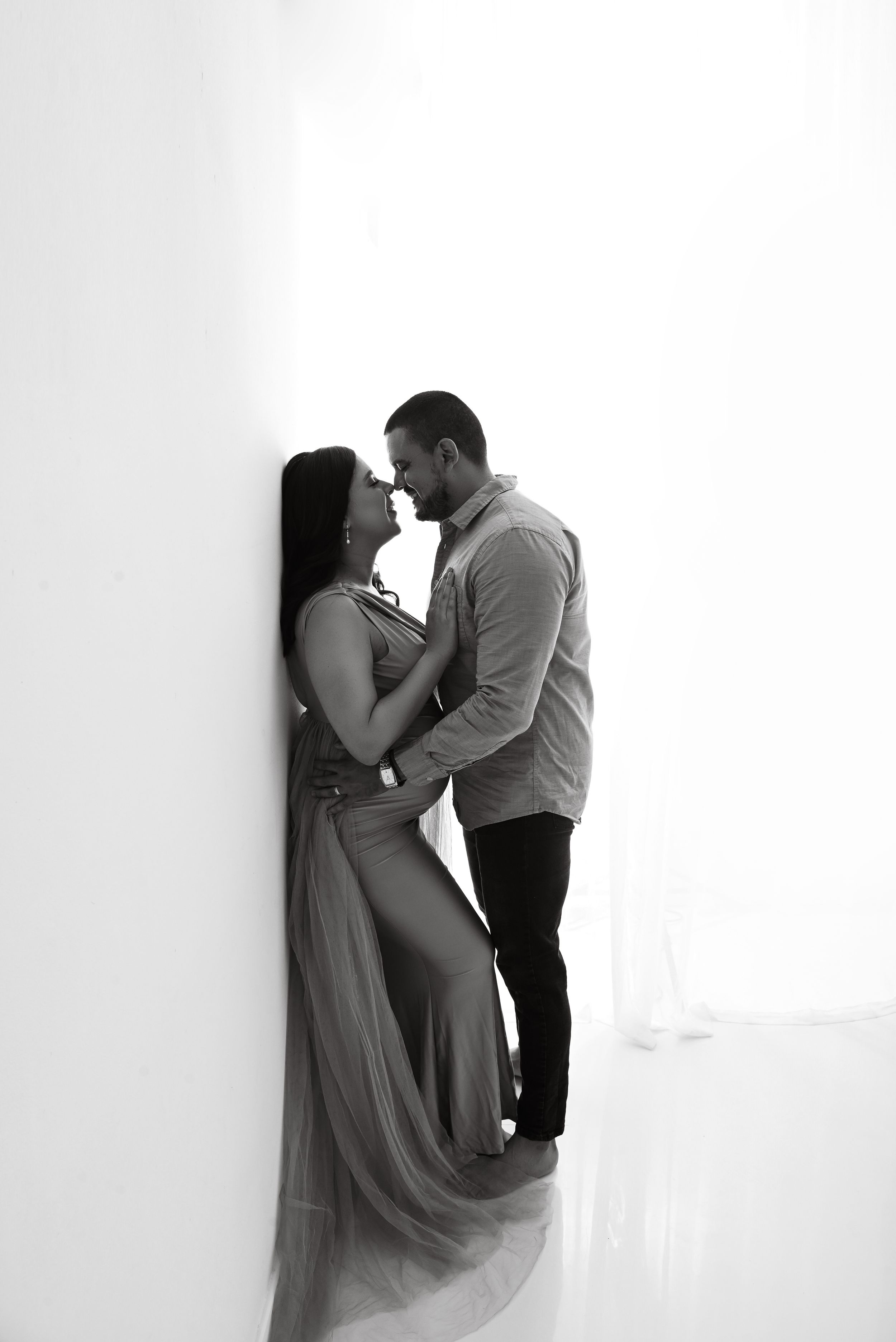 Intimate black and white maternity portrait against white wall.