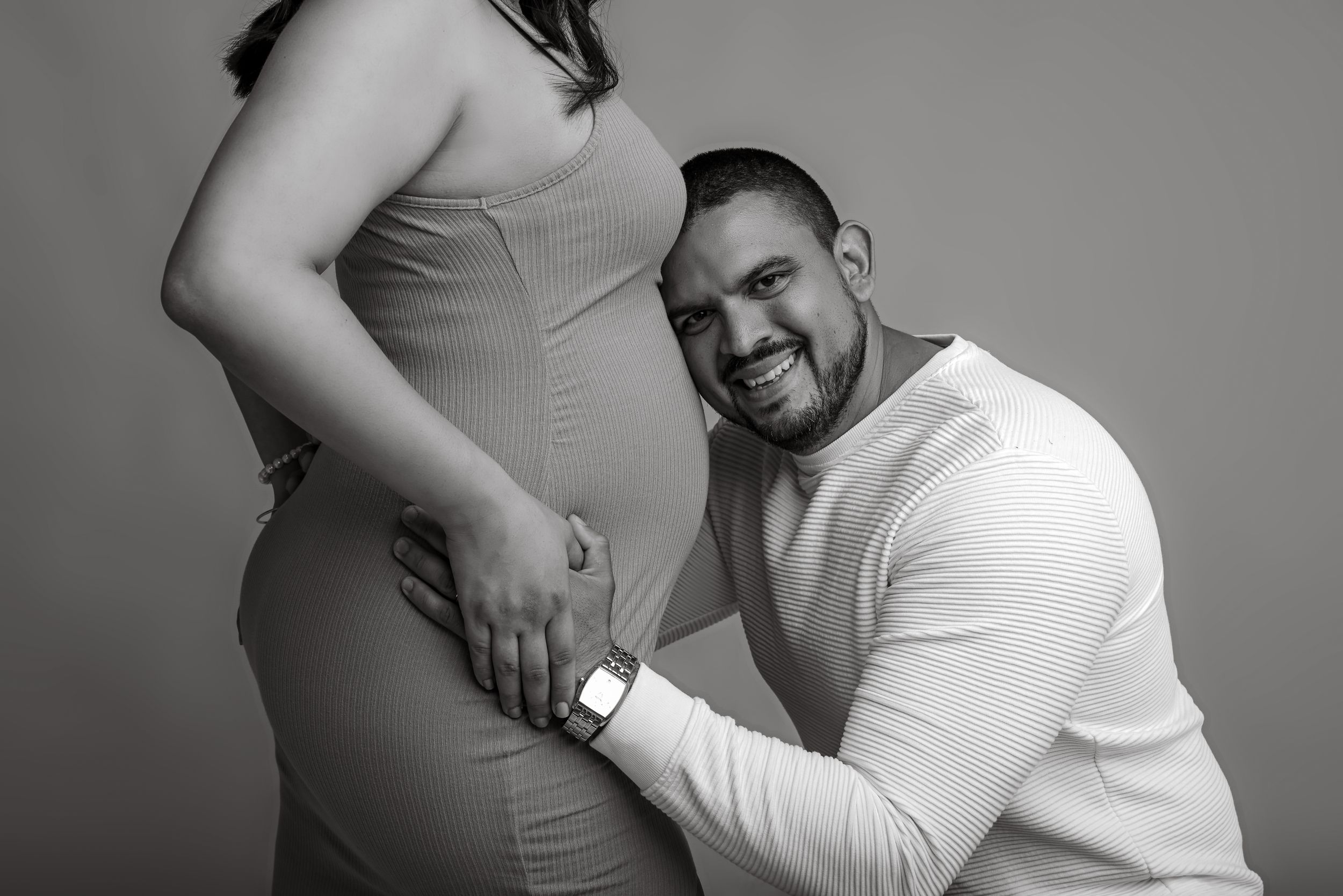 Intimate black and white maternity photo with loving partner resting head on pregnant belly.