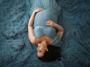Artistic overhead maternity pose on blue textured fabric backdrop.