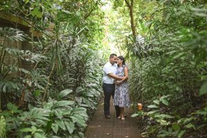Romantic maternity photo of couple walking along lush green forest path.