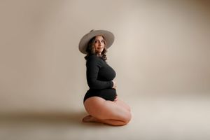 Maternity portrait of person wearing black bodysuit and wide-brim hat.