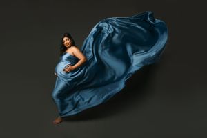 Dramatic maternity photo with flowing blue fabric against dark background.