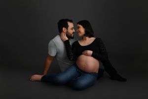 Intimate maternity portrait of couple in black and grey against dark backdrop.