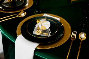 Elegant table setting with black and gold plates, green tablecloth, and white napkin #QuinceneraPartyPhotography #QuinceneraDressPhotography