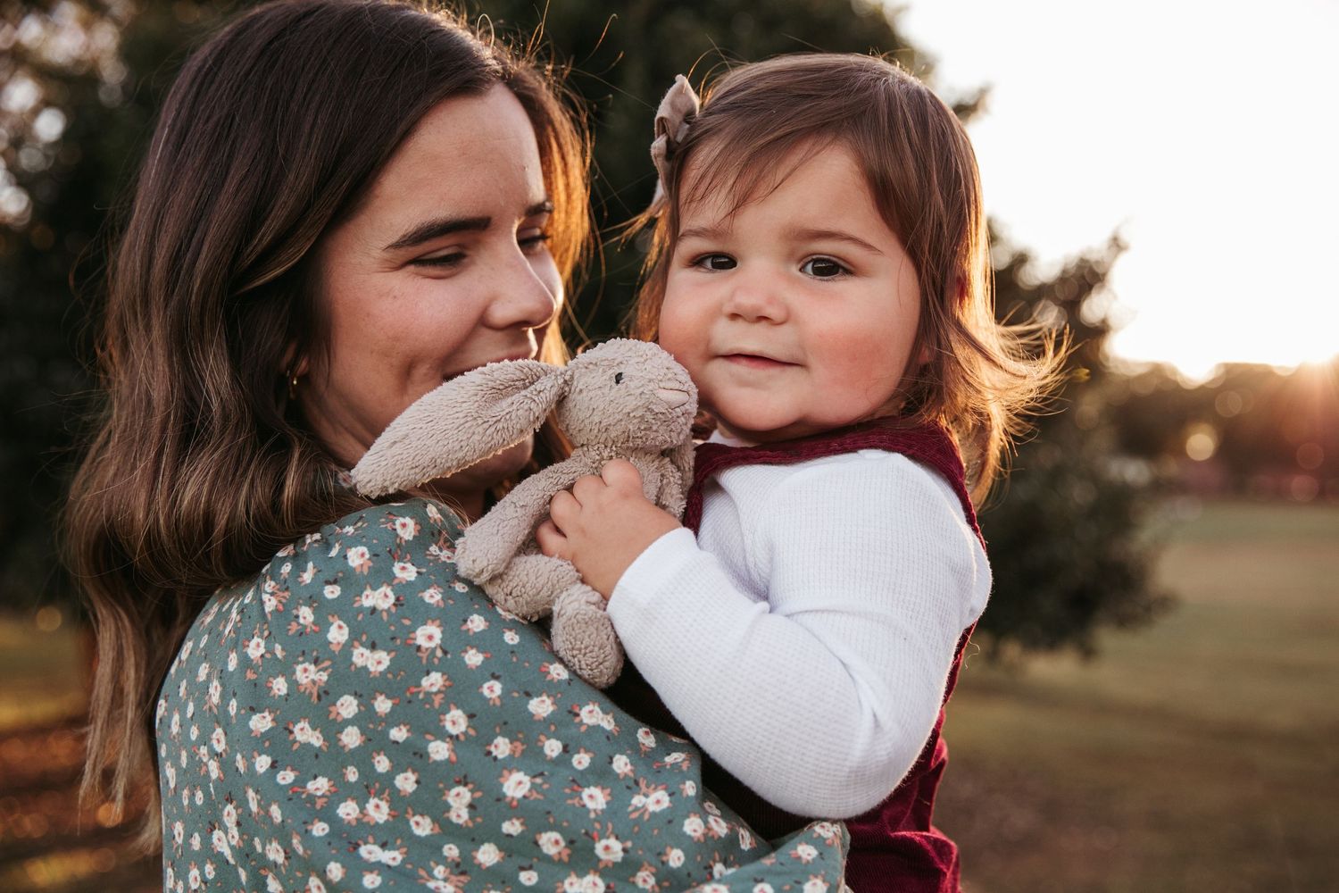 A sweet outdoor portrait showing a parent and child holding a stuffed bunny toy at sunset.