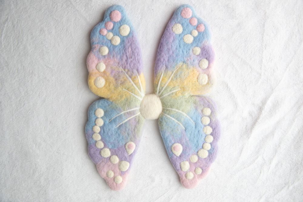Pastel rainbow felt butterfly wings with white dot details on white background.