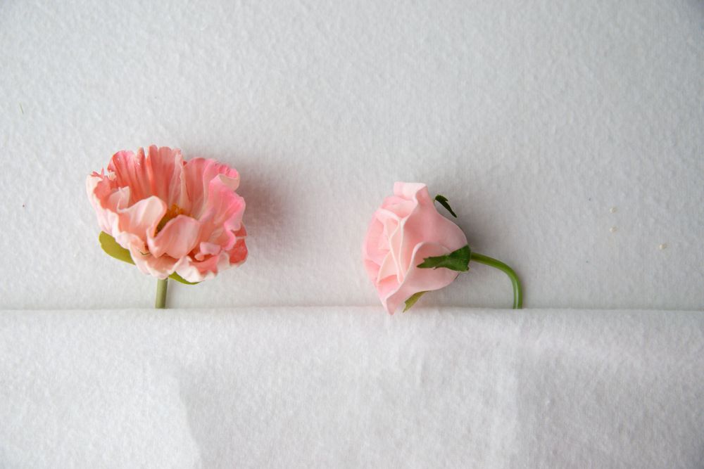 Two delicate pink paper flowers with green stems displayed against a white background.