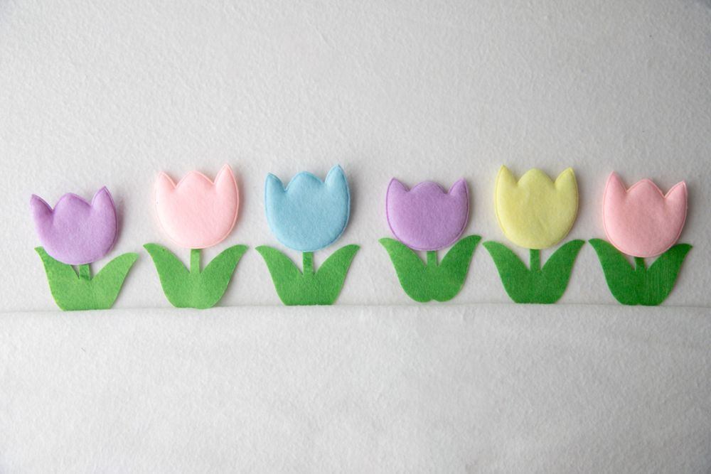 Six colorful pastel felt tulips in purple, pink, blue, and yellow arranged in a row on white felt.