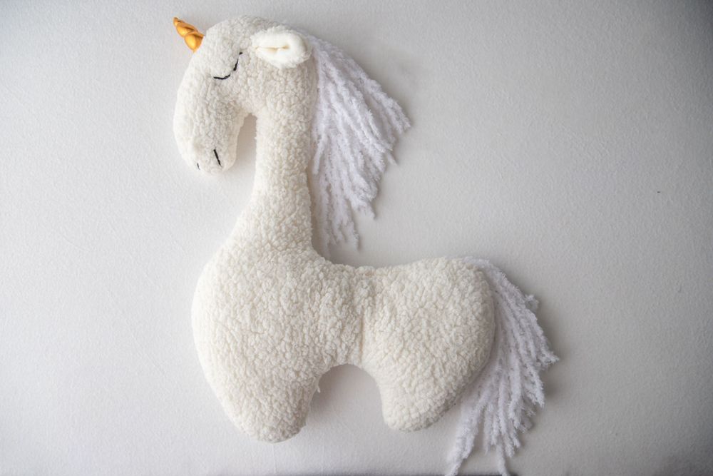 White fluffy unicorn stuffed animal toy with golden horn and yarn mane on white background.