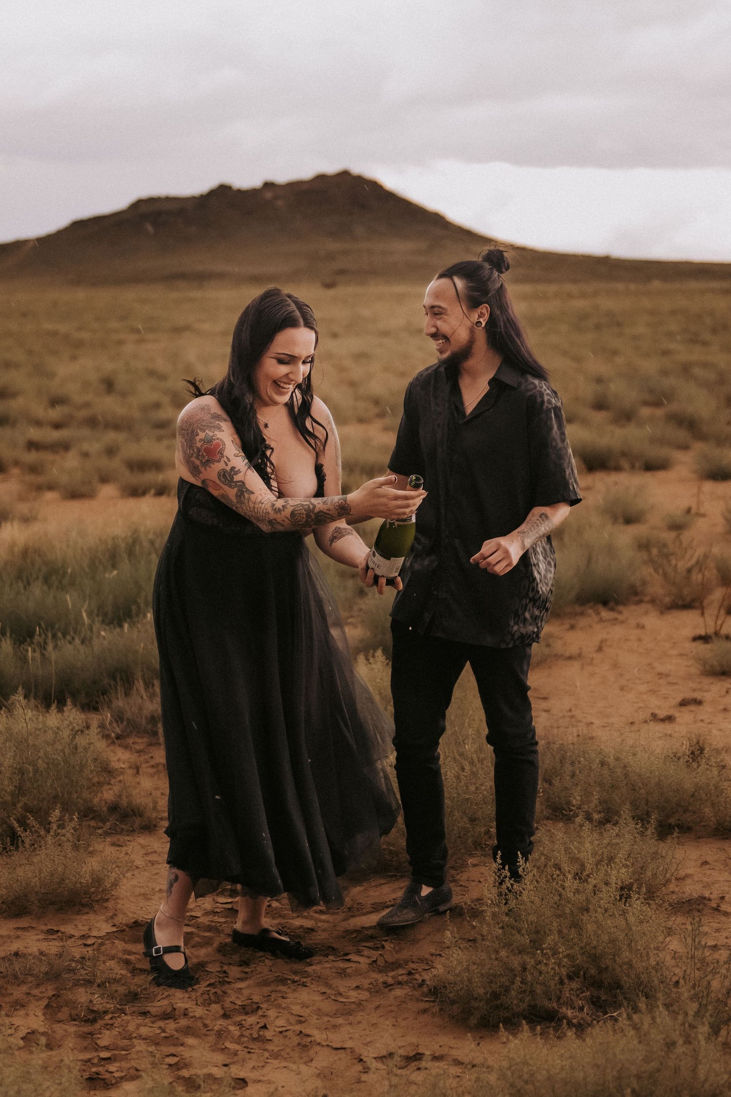 A joyful couple shares a candid moment laughing together in the desert with mountains in the background. Albuquerque engagement photographer