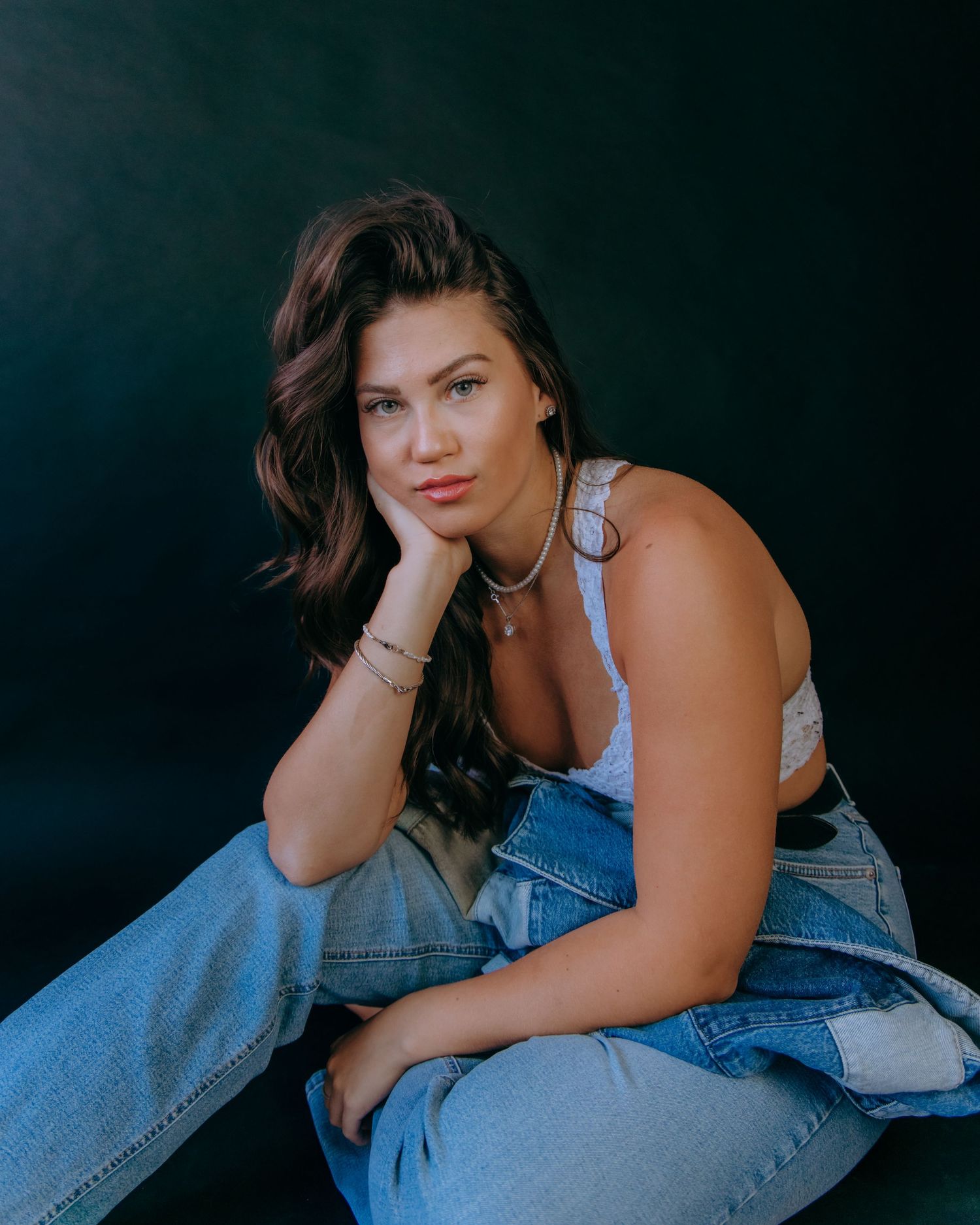 Person in denim outfit posing against dark background for moody portrait series.