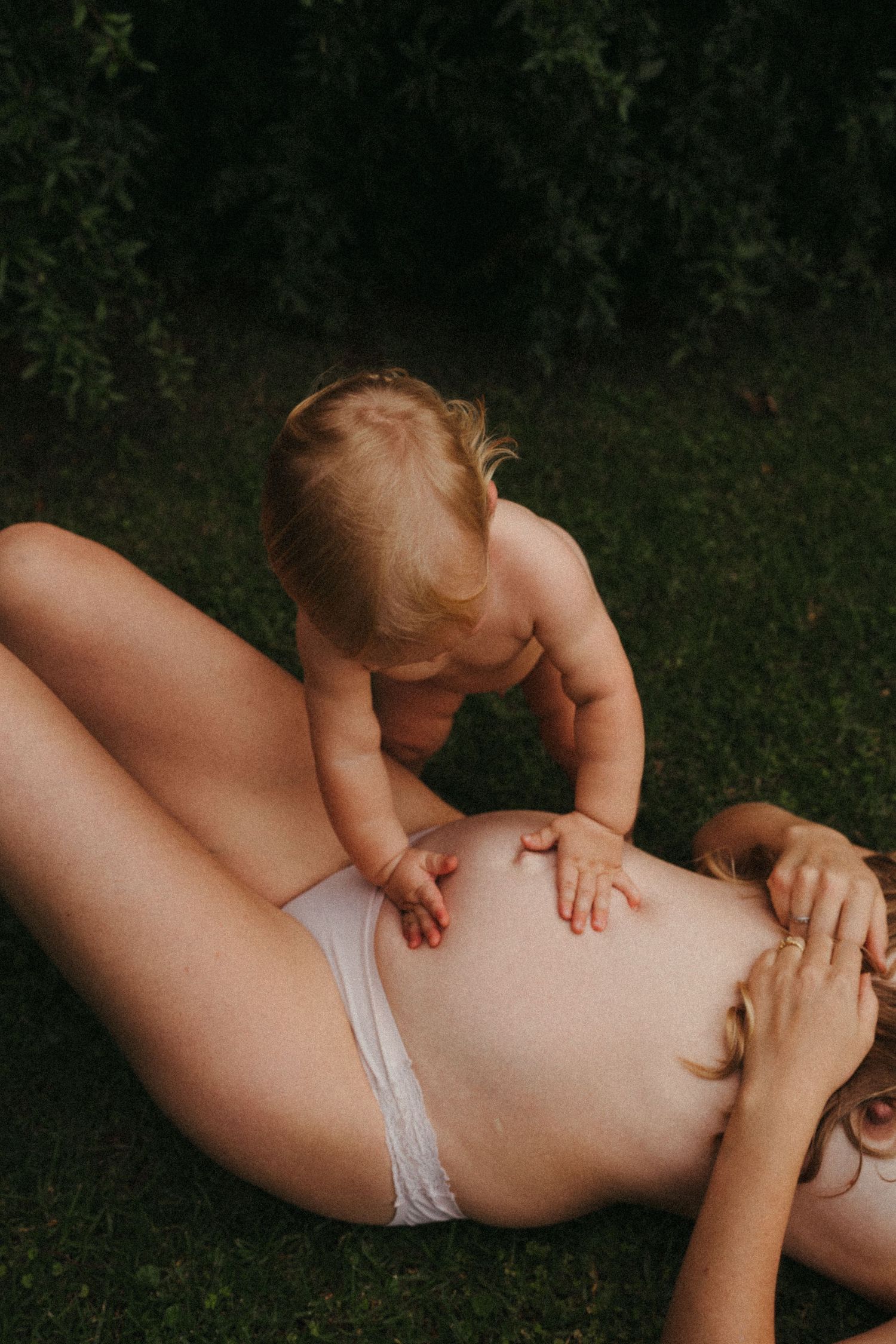 a toddler playing on his mothers bare pregnant belly
