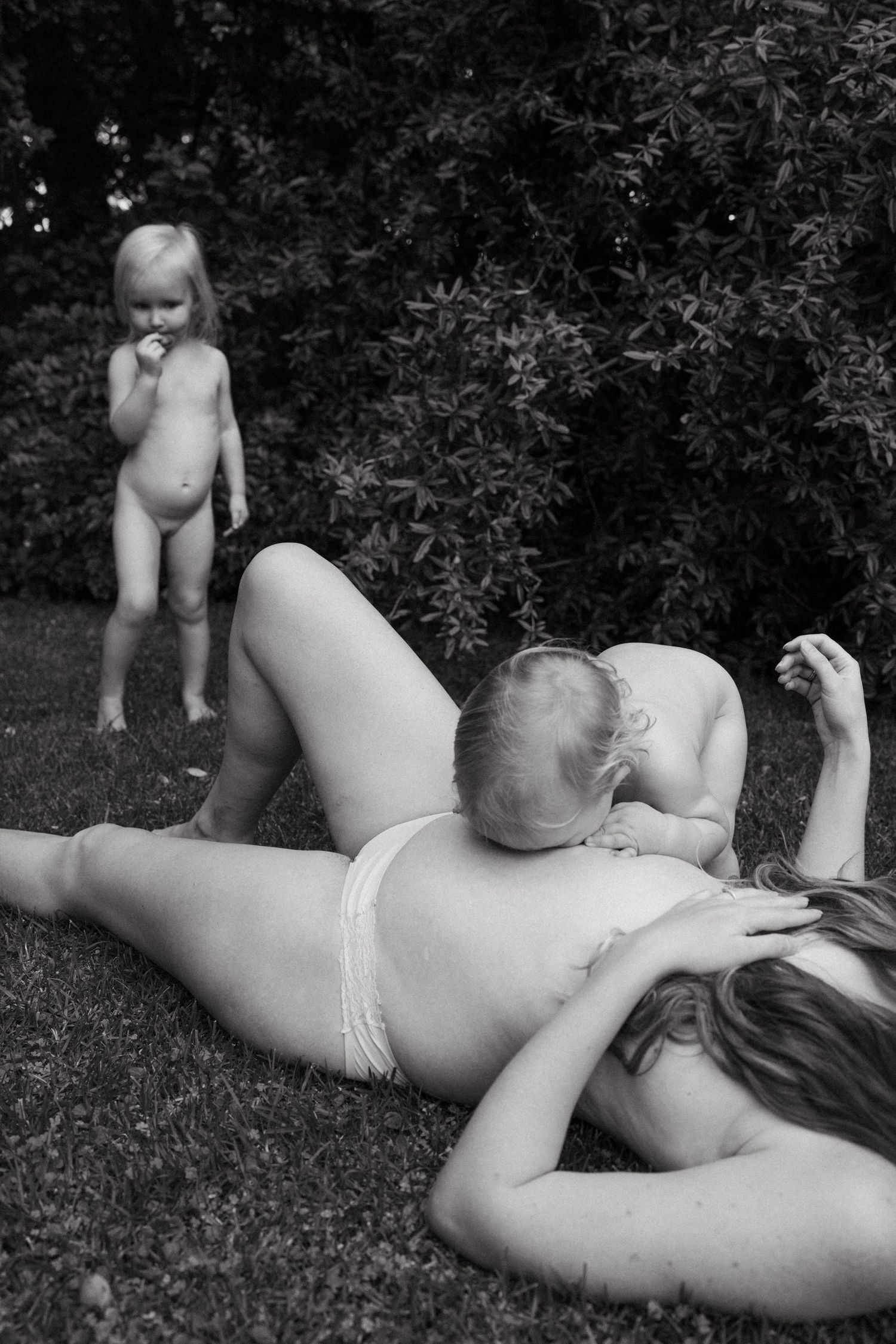 A tender black and white photo of a family lounging together on grass in summer.