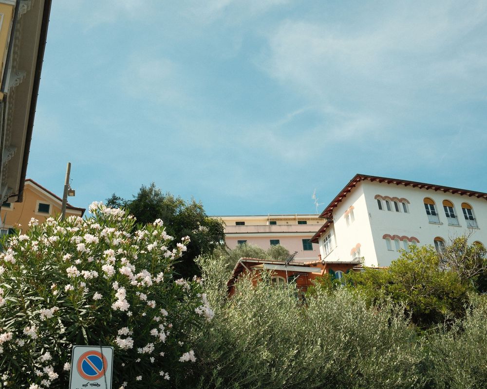 A panoramic view of a Mediterranean coastal town with white buildings and lush greenery against a blue sky.