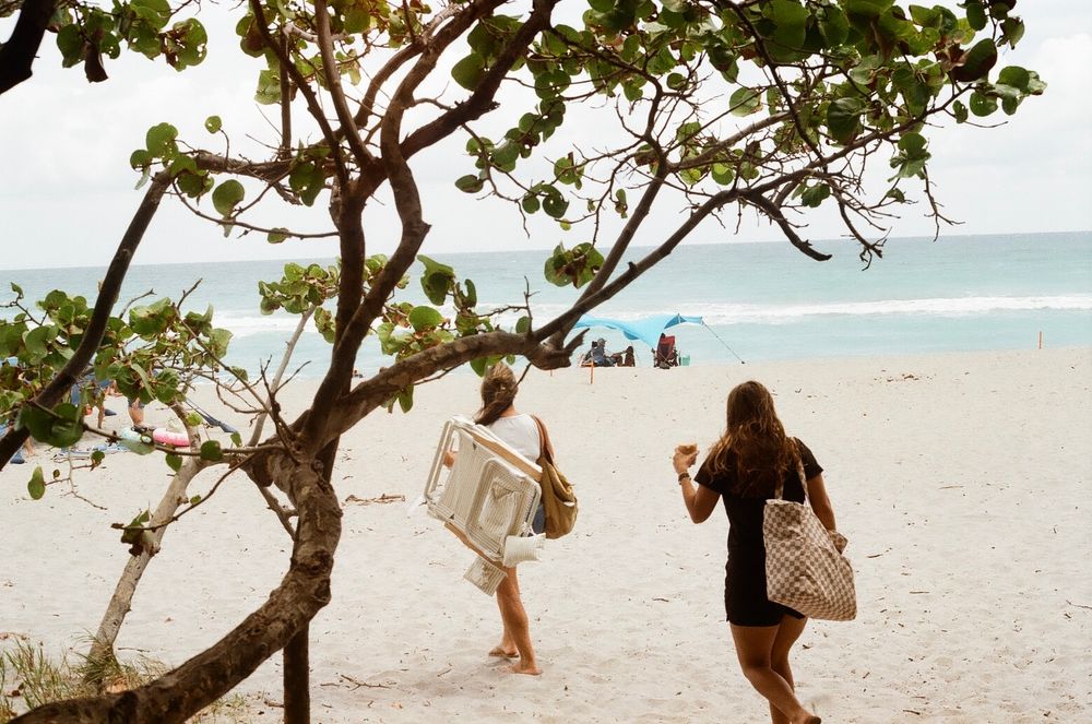 People walking and relaxing under palm trees on a tropical beach with white sand and turquoise water.