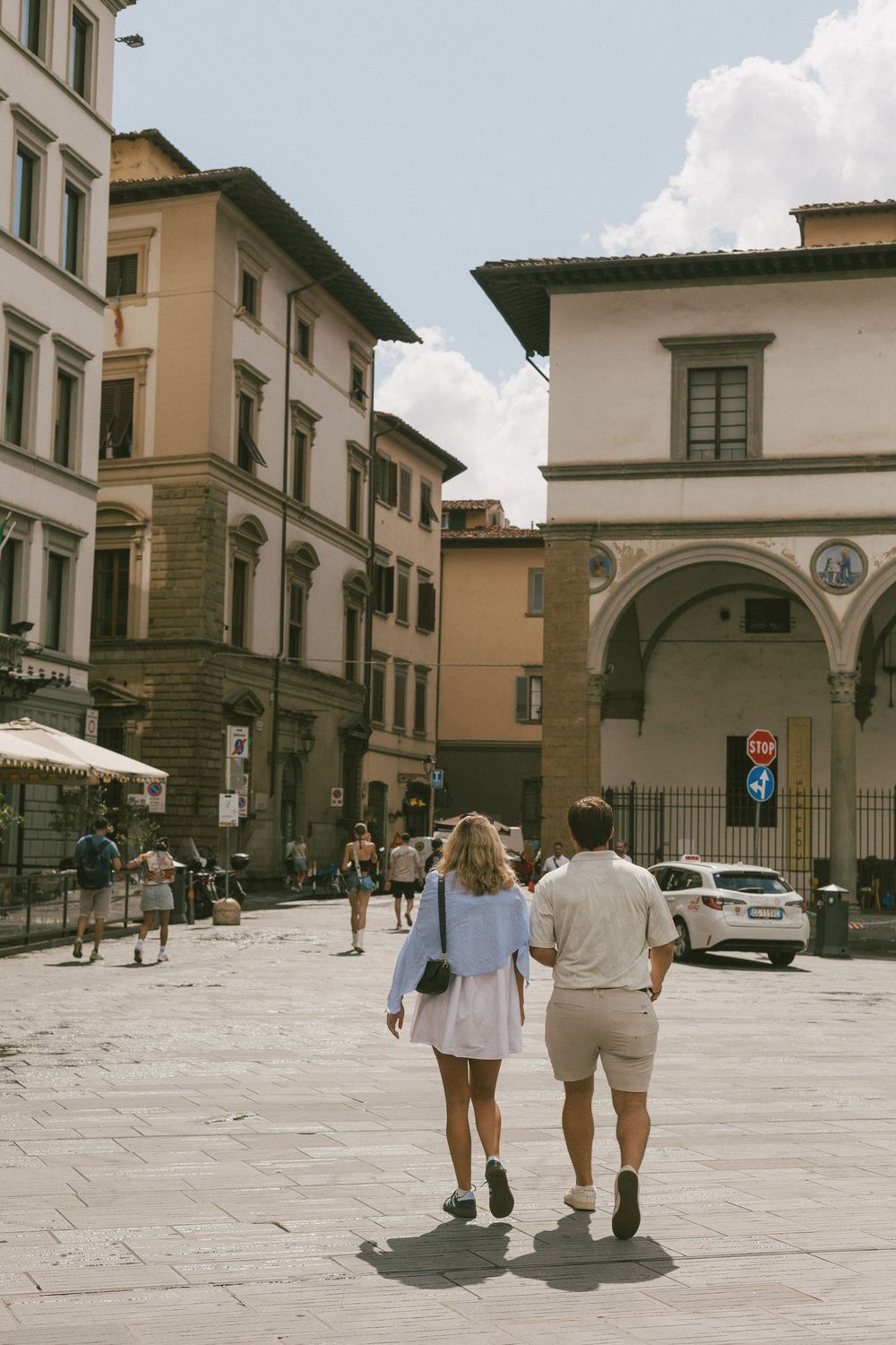 People walking along a historic Italian street with beige buildings and arched architecture in Florence.