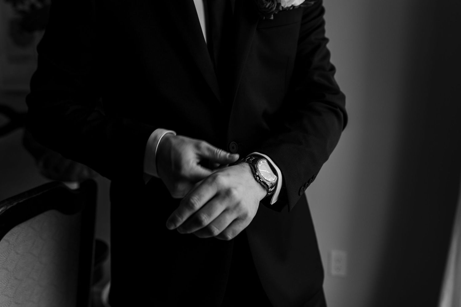 Monochrome image showing hands adjusting a necktie against dark suit fabric.