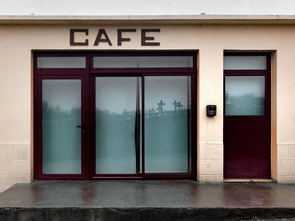 A minimalist storefront with 'CAFE' signage and dark-tinted windows along a beige commercial building exterior.
