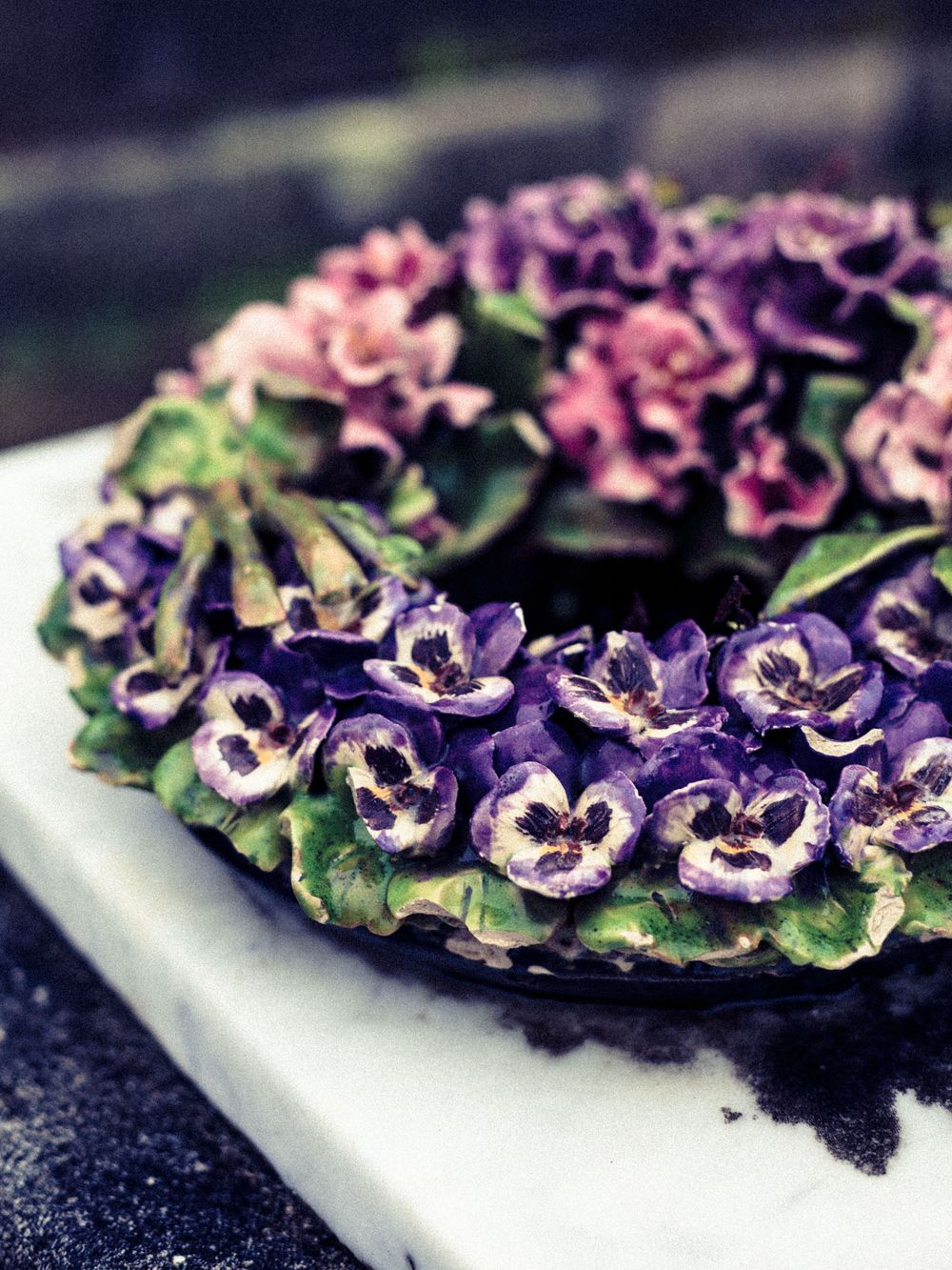 Purple and pink decorative flowers arranged in a circular pattern on a white plate against a dark background.