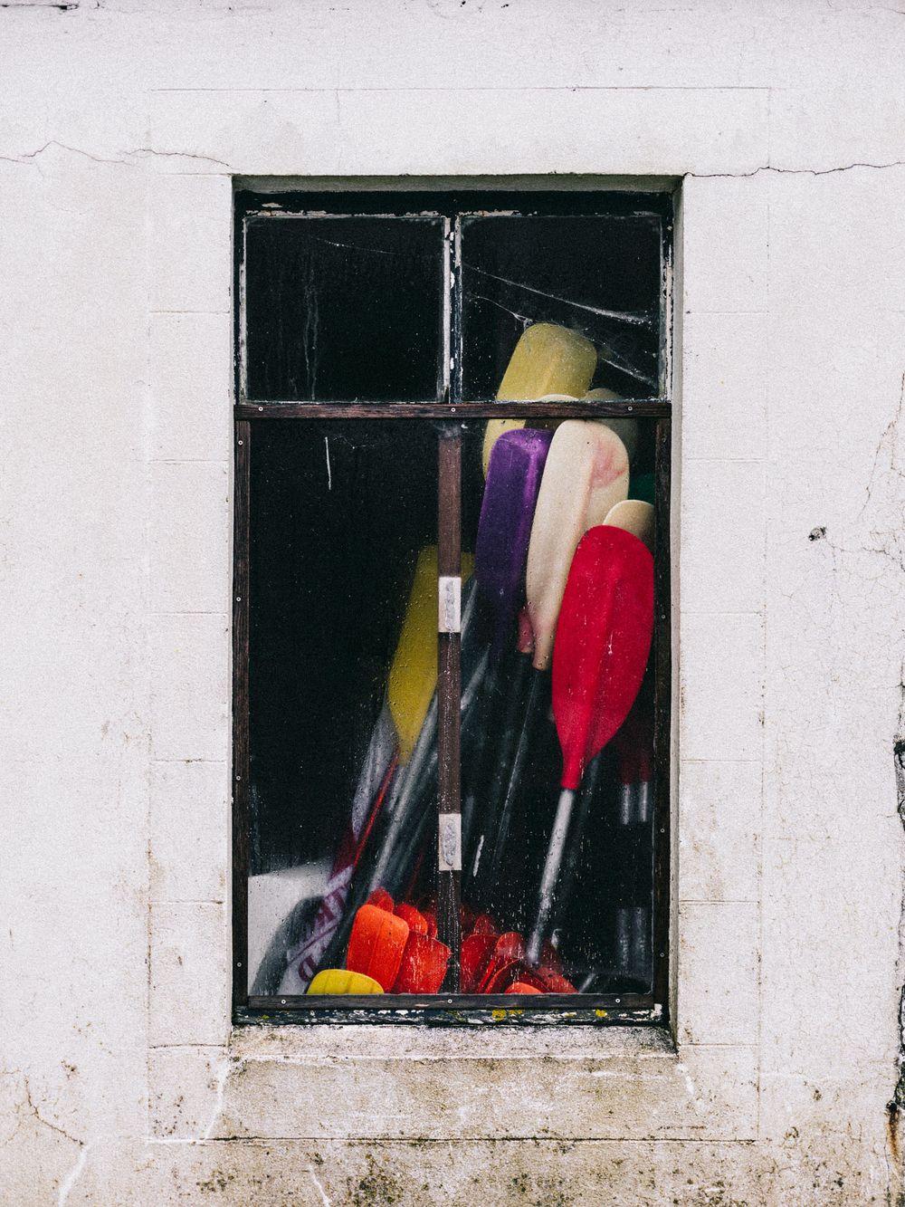 Colorful cleaning supplies including brooms and brushes are visible through a small window in a white wall.