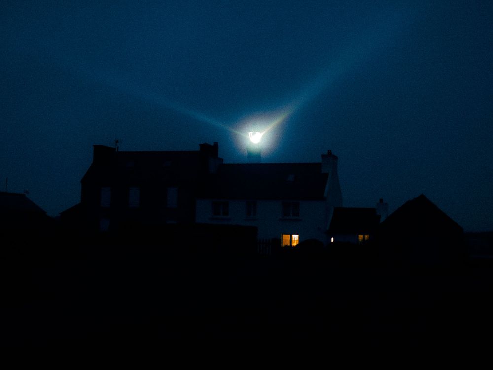 A bright meteor streaks across a dark night sky above silhouetted buildings creating a dramatic celestial display.