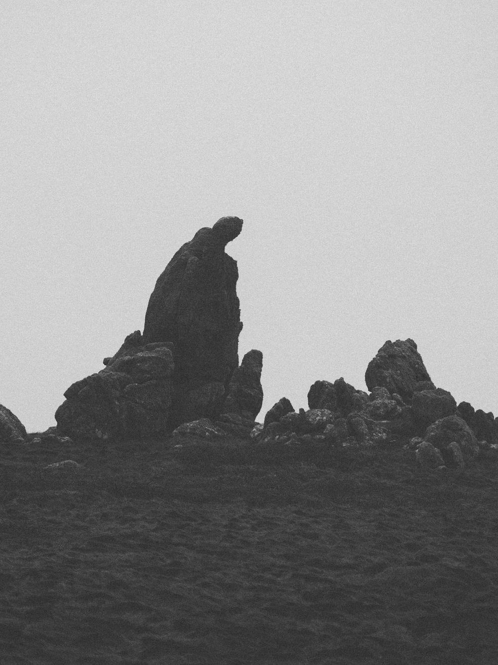 A dramatic black and white silhouette of jagged rock formations against a light sky creates a moody landscape scene.