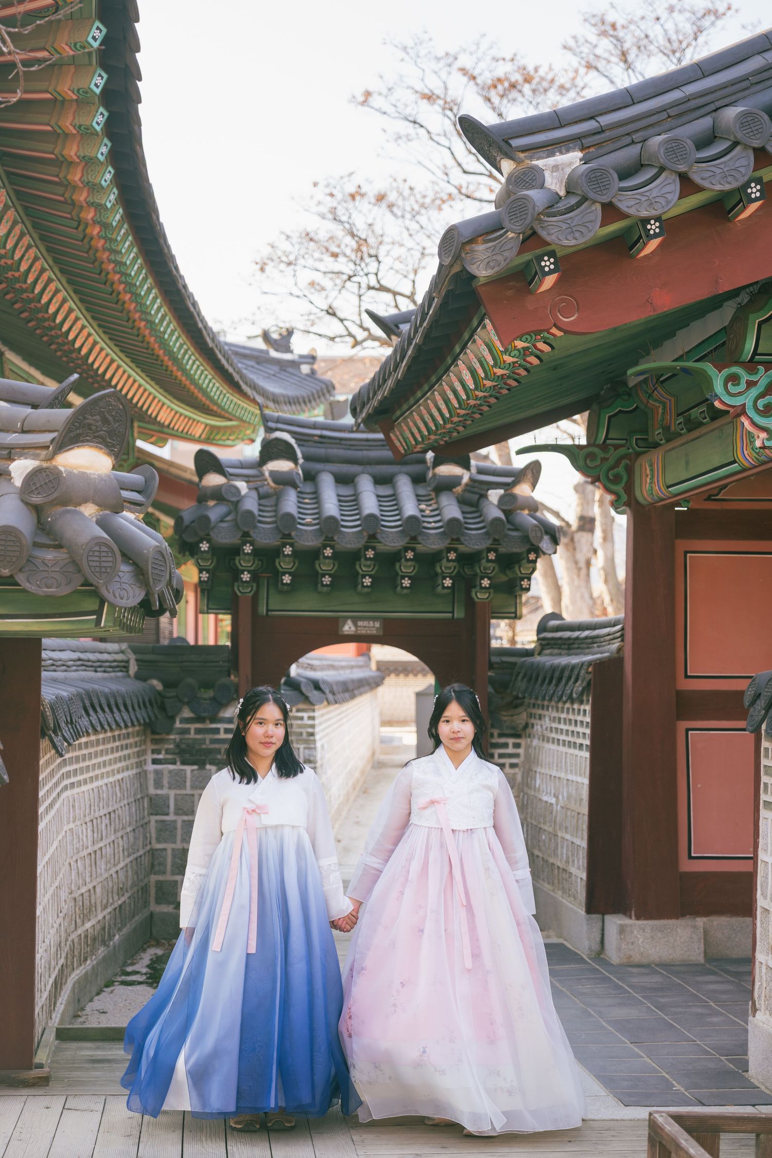 Traditional Korean hanbok dresses displayed in front of ornate temple architecture with curved tile roofs and stone walls.