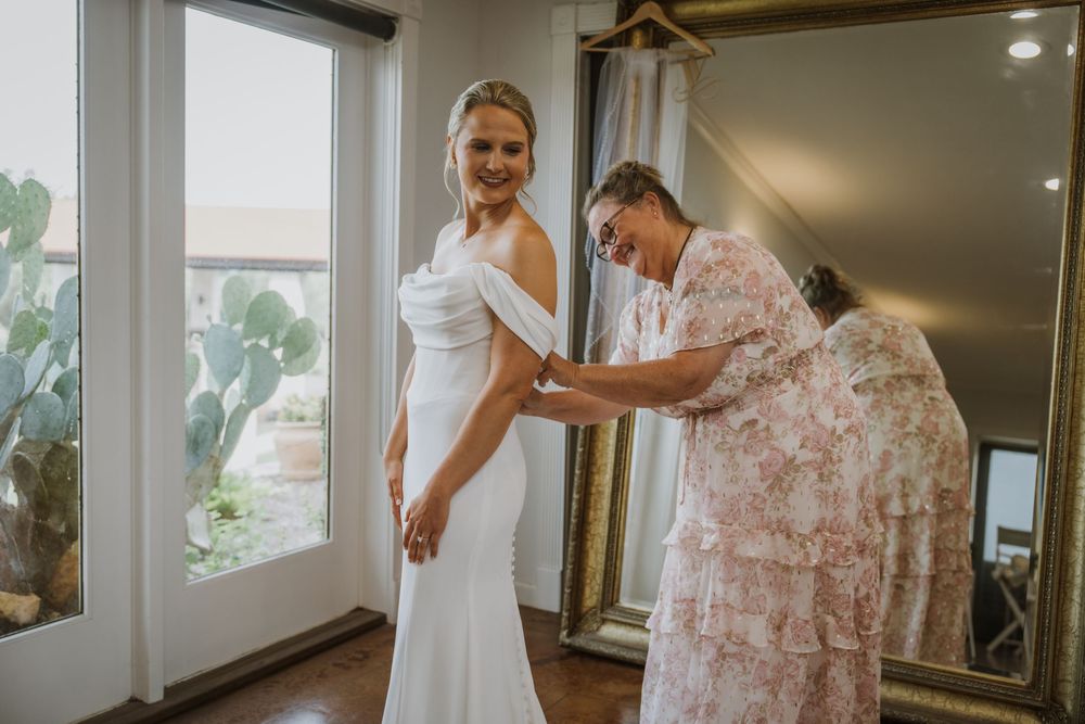 Wedding dress fitting scene in a sunlit room with elegant white gown.