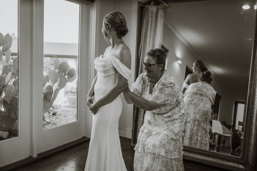 Black and white photograph of a wedding dress fitting moment.