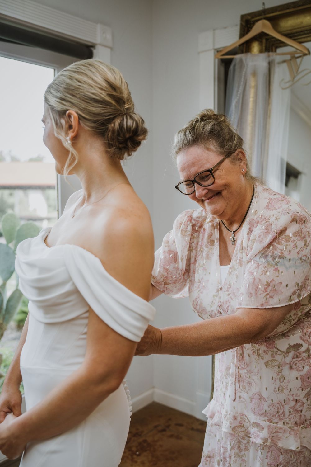 Intimate wedding dress preparation moment in a bright interior setting.