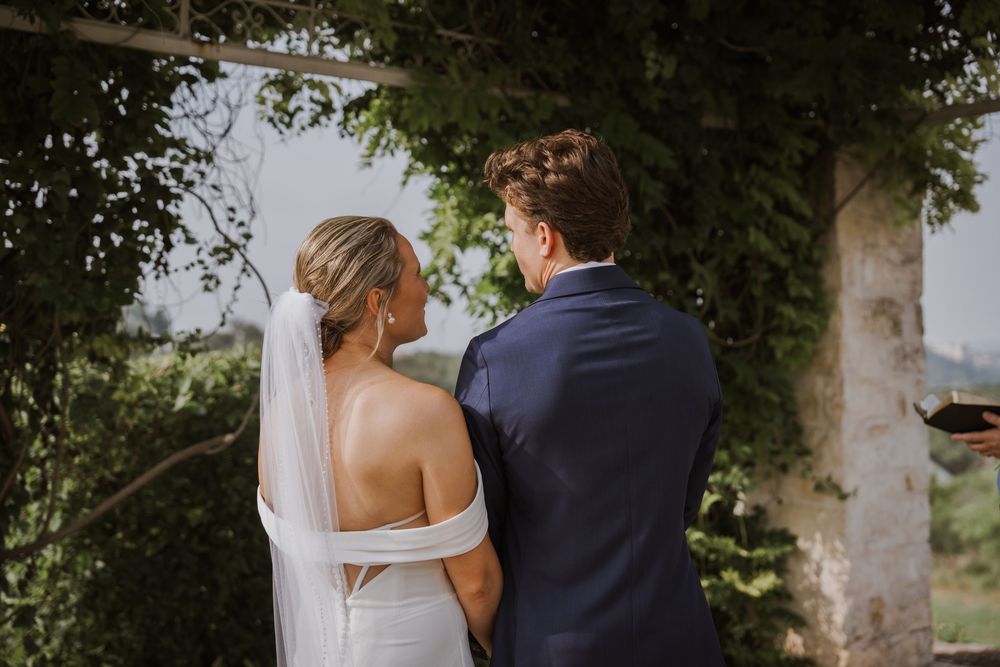 A couple embraces during their outdoor wedding photo session surrounded by greenery.