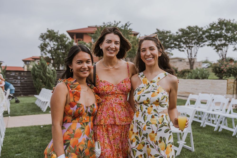 Bridesmaids in colorful floral dresses gather for photos at an outdoor wedding.
