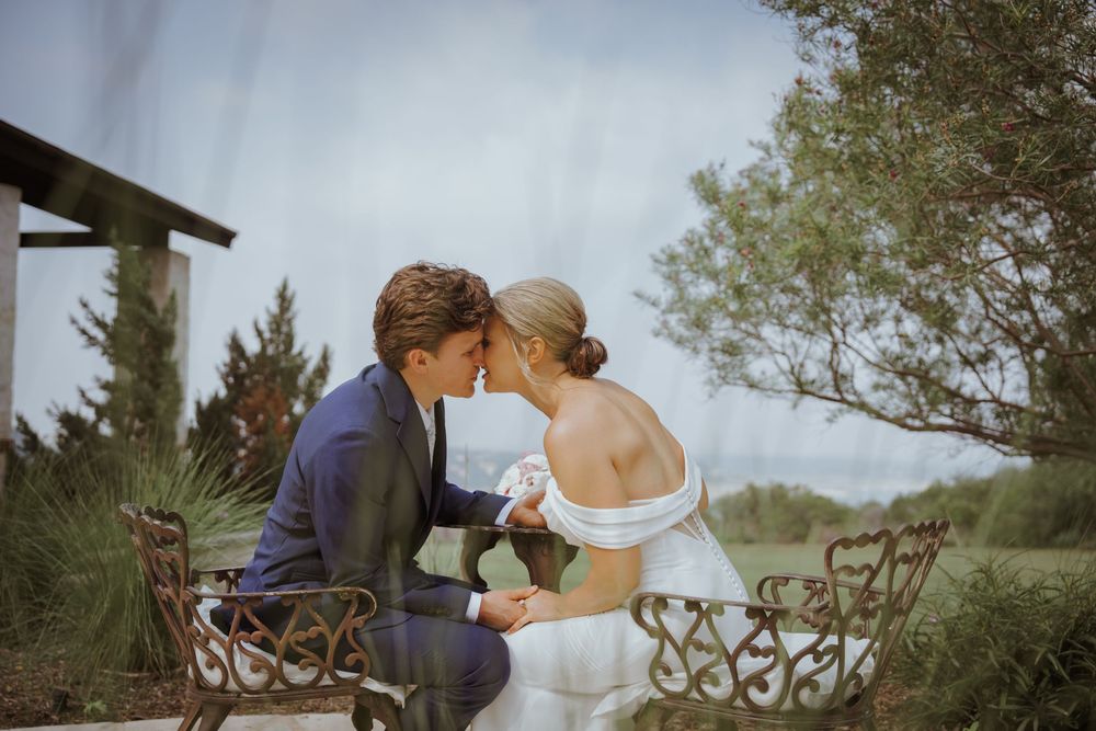 A romantic wedding moment captured against a cloudy sky with ornate metalwork details.