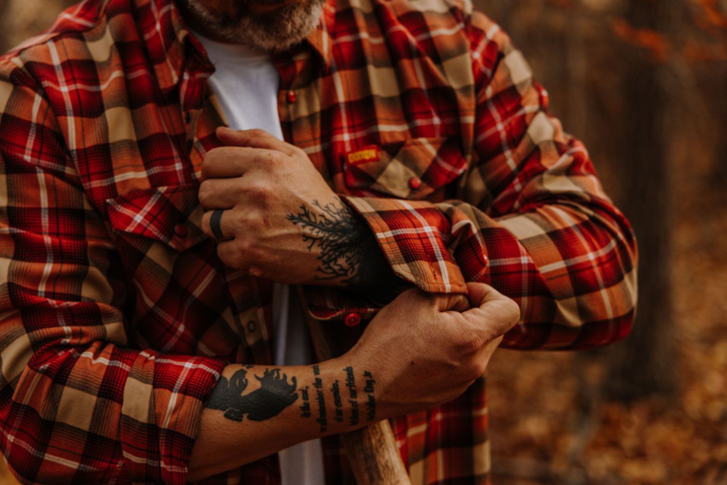 Person in red plaid flannel shirt holds smartphone outdoors during autumn season.