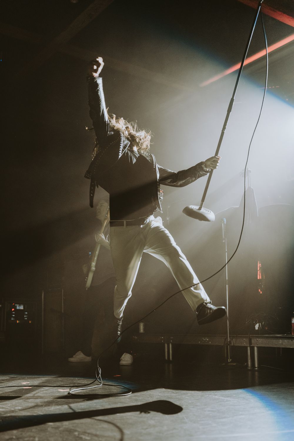Performer jumps energetically on stage during dramatic concert moment with spotlight effects.