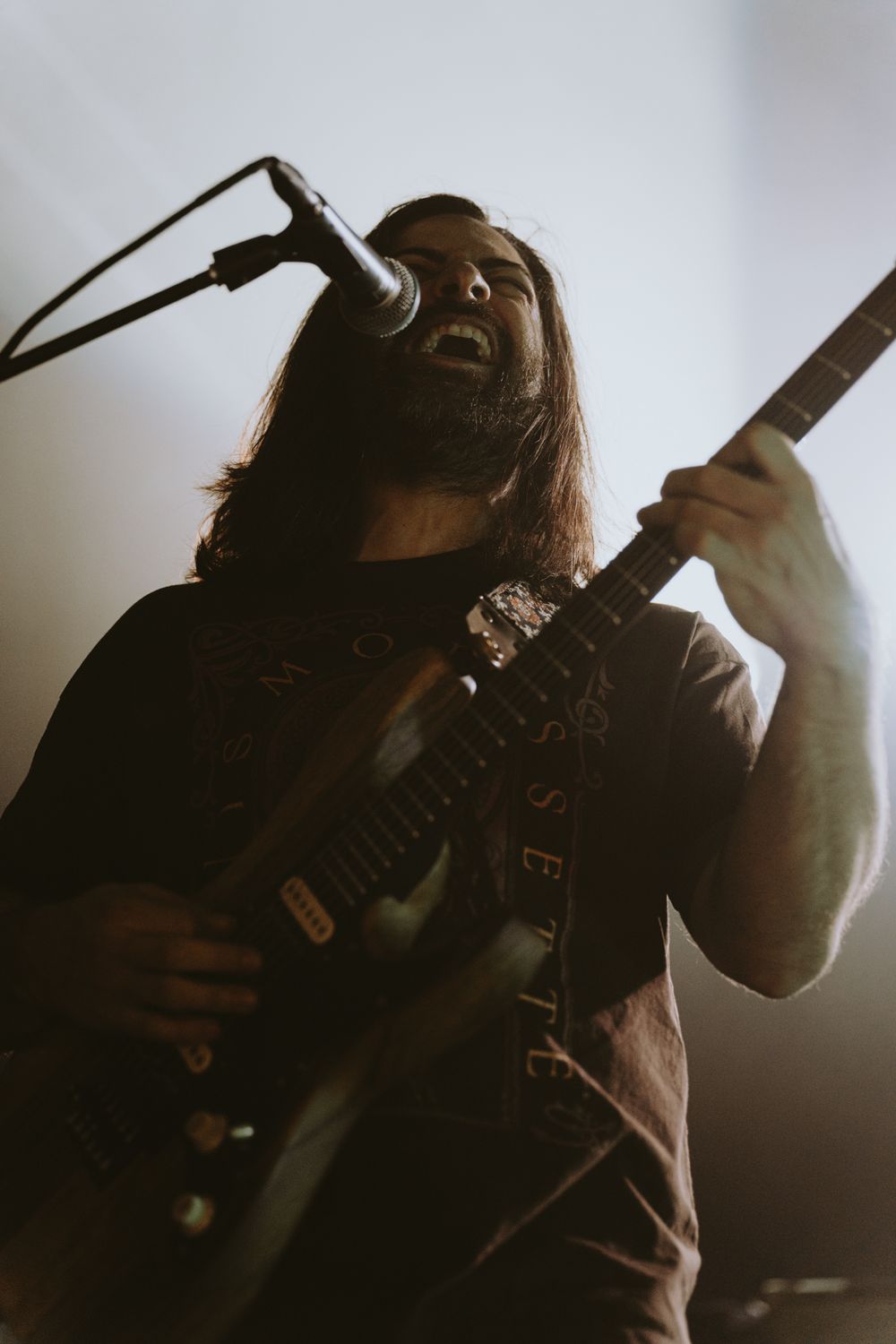 Guitarist plays and sings with intense expression during dark moody concert performance.