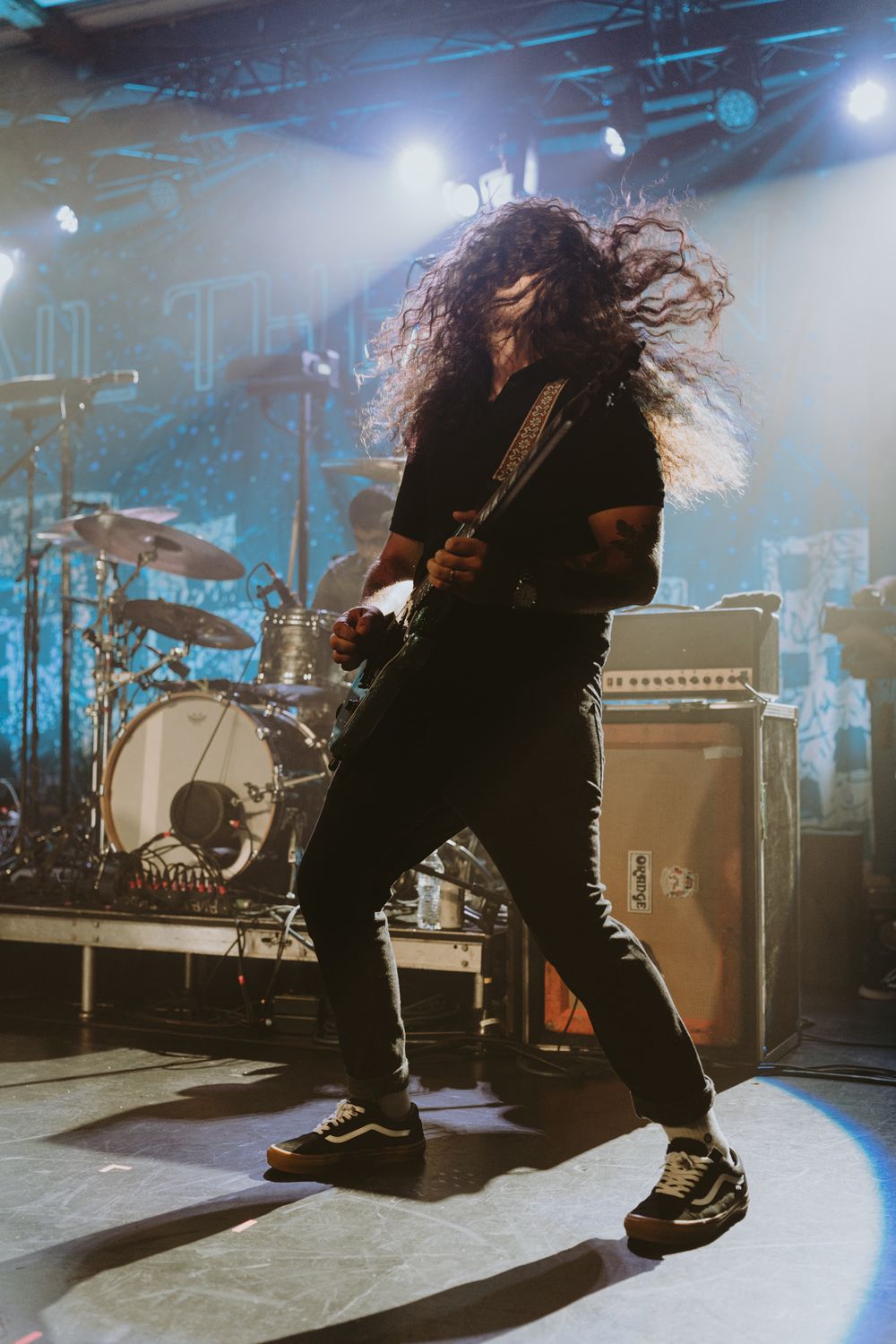 Rock musician with flowing hair plays guitar energetically on concert stage.