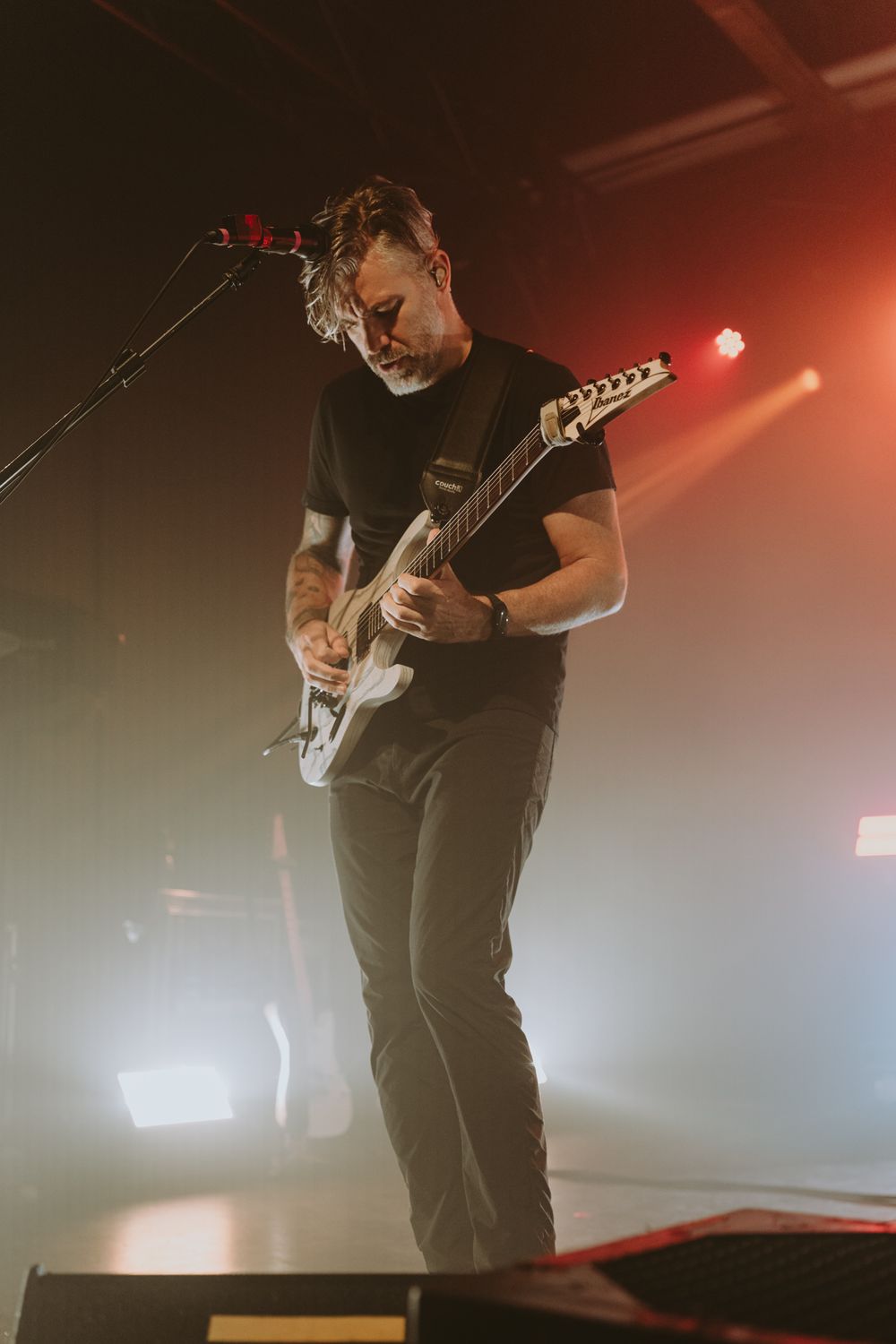 Guitarist performs on stage with electric guitar in dramatic red lighting during live concert performance.