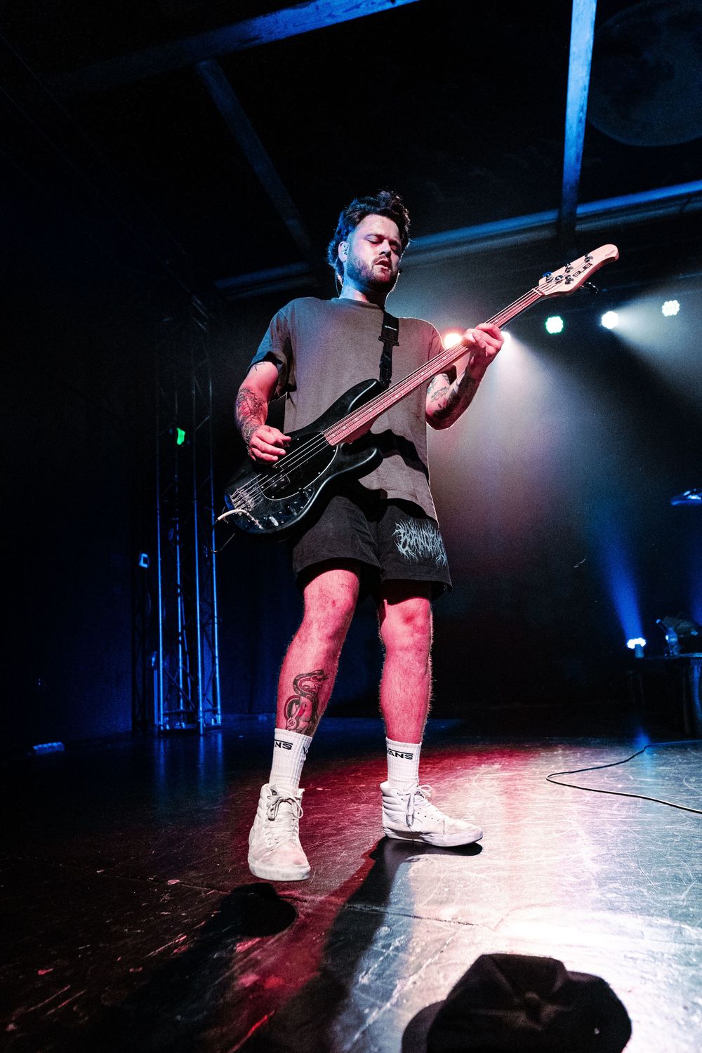 Performer on stage jumping energetically in black attire and white boots under dramatic blue lighting.
