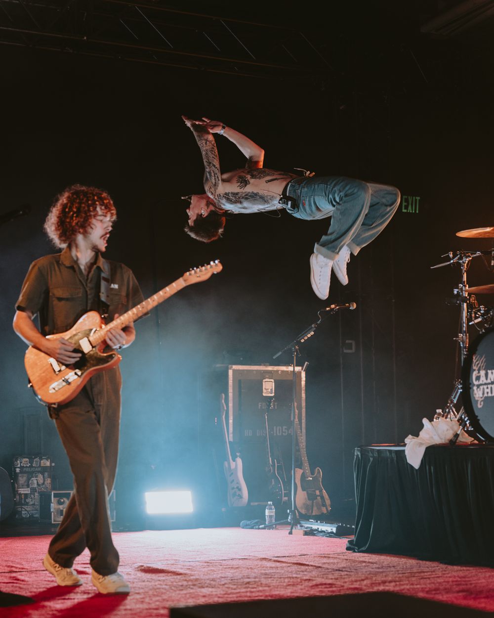 Dynamic concert scene with guitarist playing while performer executes mid-air backflip.
