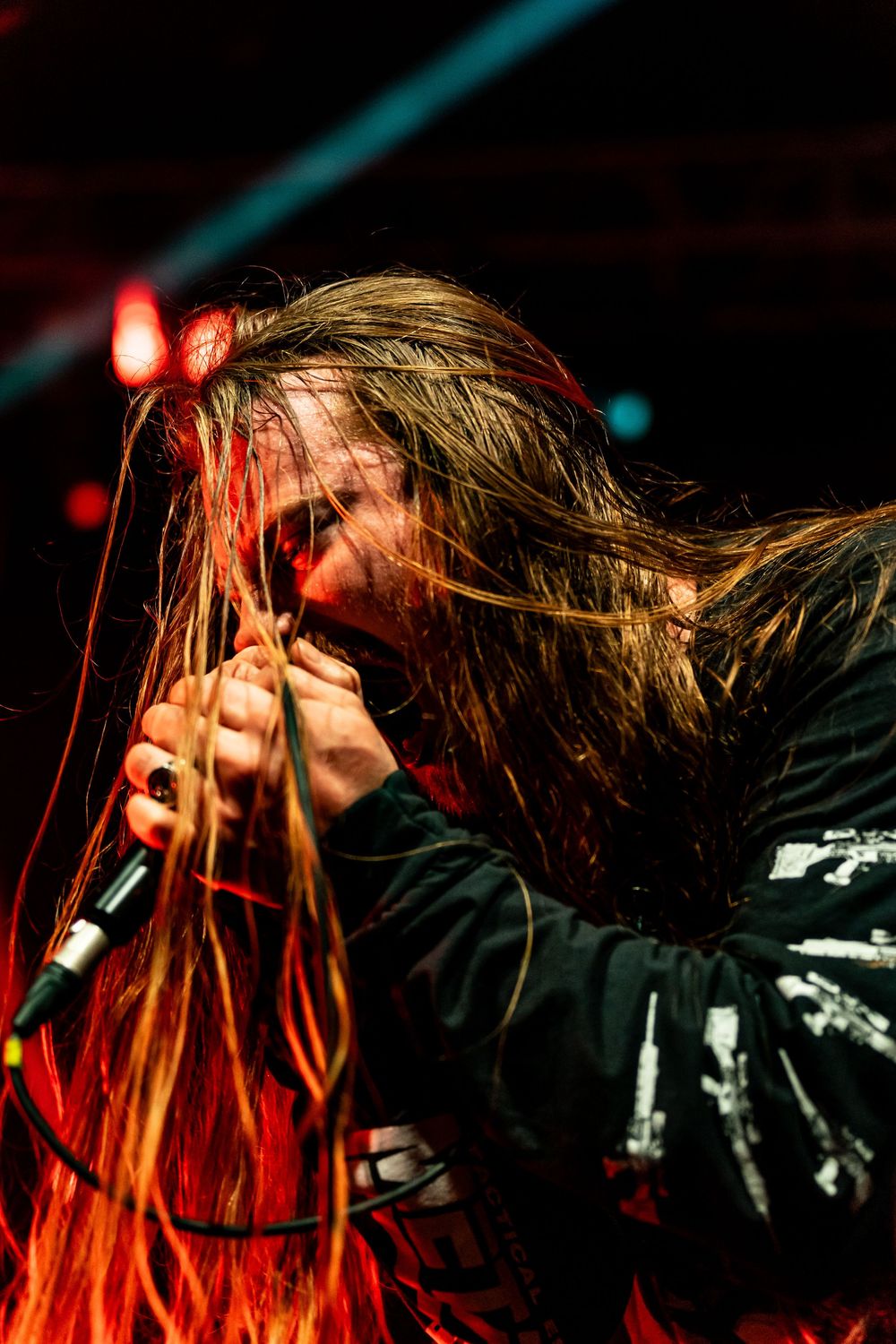 Heavy metal vocalist performing passionately with long hair under red stage lighting.